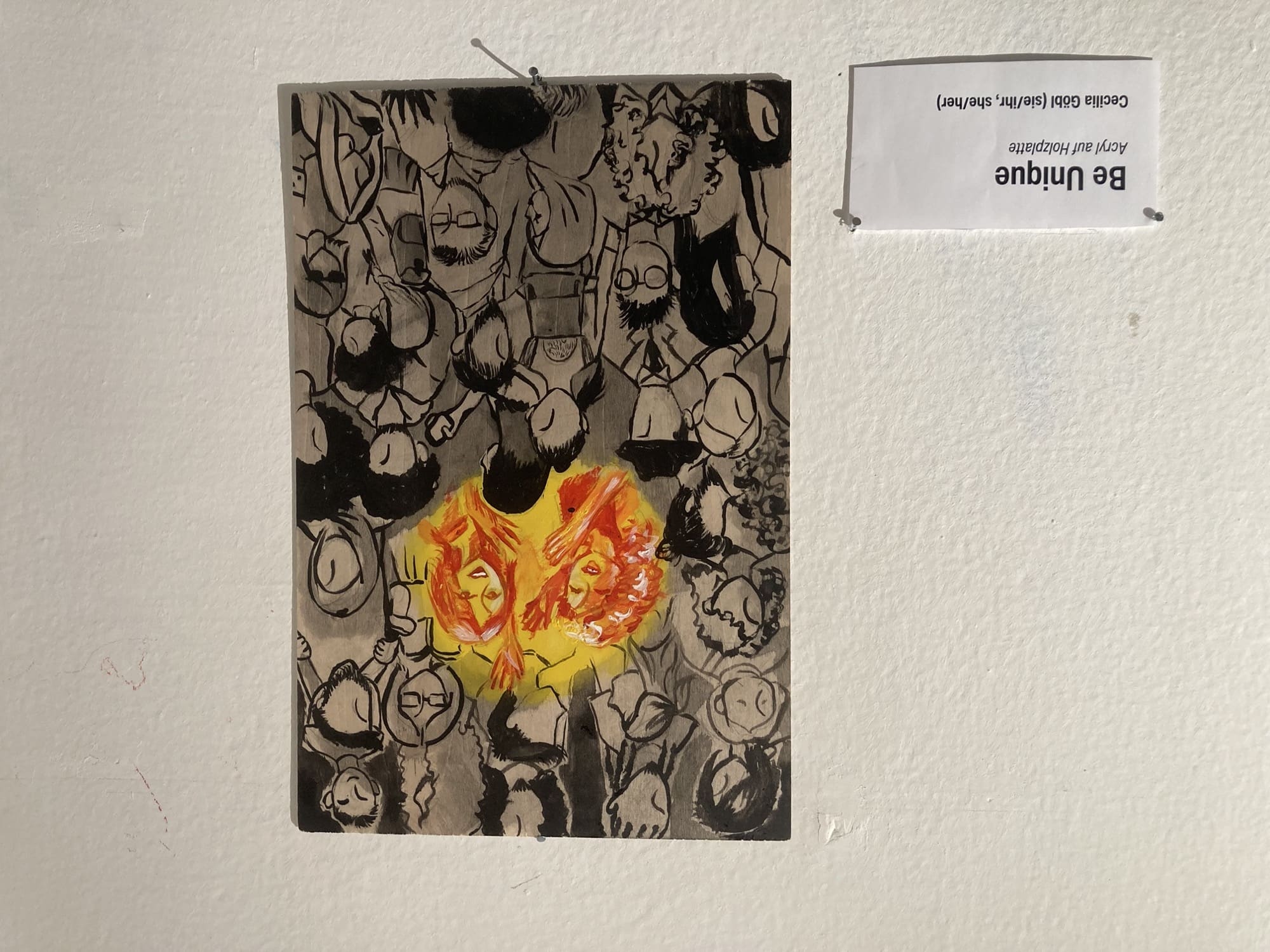 ein Bild an der Wand zeigt zwei glückliche gebärdende Menschen, gemalt in Rot-Gelb-Orange-Tönen in einer Menge an grau-schwarzen Menschen, die allesamt keine Gesichtszüge haben