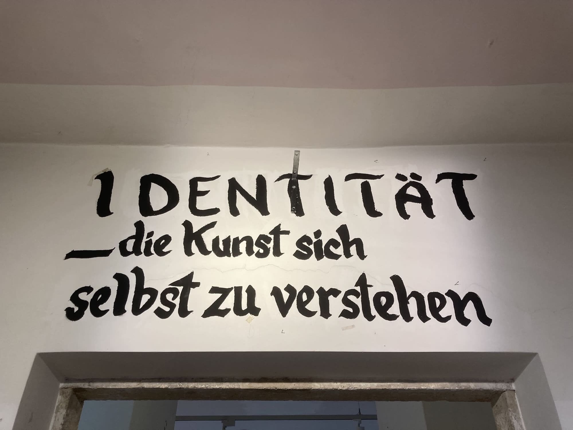 Schriftzug, in schwarzer Farbe auf eine Wand über einer Tür gemalt: „Identität – die Kunst sich selbst zu verstehen“